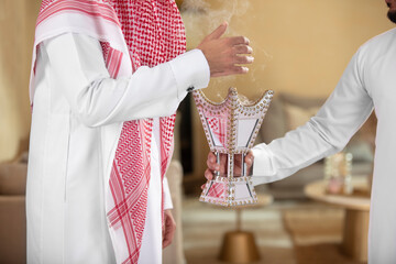 An Arab man holds a censer for his guesr perfumes him with it - obrazy, fototapety, plakaty