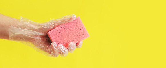 A pink sponge for washing dishes in a woman hand on a yellow background. A hand in a transparent...