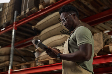 Fototapeta na wymiar Side view portrait of young African American man holding digital tablet at warehouse in coffee roastery, copy space