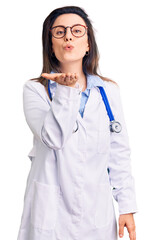 Young beautiful woman wearing doctor stethoscope and glasses looking at the camera blowing a kiss...