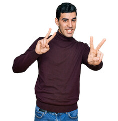 Fototapeta premium Handsome hispanic man wearing casual turtleneck sweater smiling looking to the camera showing fingers doing victory sign. number two.