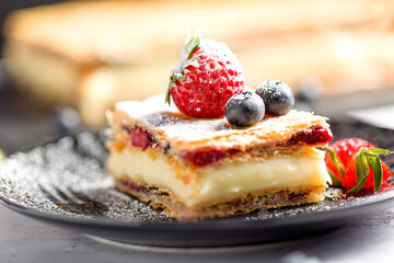 A piece of Napoleon cake with poppy seeds and cherries, decorated with strawberries, blueberries on a light background. Close up