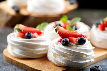 The process of making Pavlova dessert. Pavlova dessert with fresh slices of strawberries, blueberries and mint leaves on a gray background - obrazy, fototapety, plakaty
