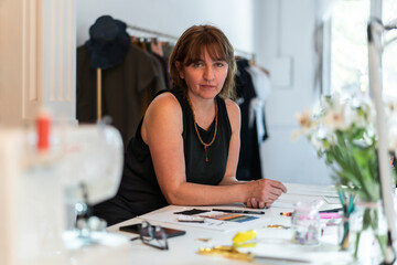 Female fashion designer looking at camera while leaning on her desk at her studio.