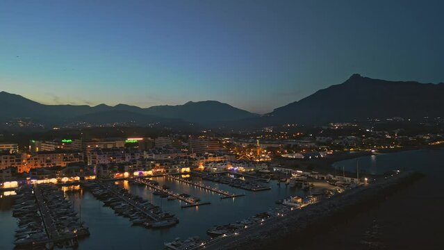 Establishing aerial panoramic view of Puerto Banus marina luxury port Marbella illuminated, Costa del Sol coastline Spain at blue hour. Travel vacation holidays in Spain
