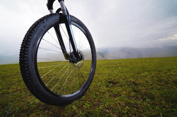 Fototapeta na wymiar Mountain biker standing on a hill or field, close-up of a wheel. Active and sports recreation concept