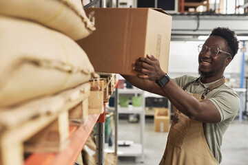 Side view portrait of smiling Black man picking up boxes from shelves in warehouse, copy space