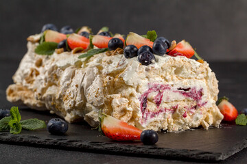 Meringue roll decorated with creamy cream and slices of fresh strawberries in a cut and blueberries.