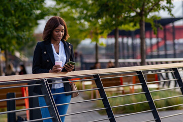 In a tranquil moment, the businesswoman of color leans against the railing, savoring the river's picturesque view.