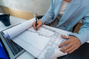 In a close-up shot, hands carefully scrutinize business statistics on a chart, highlighting her...