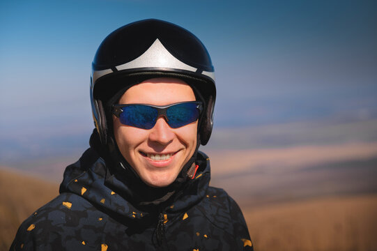 Portrait of a smiling young man with a parachute in a field. A guy paraglider in sportswear and a helmet is preparing for a flight or after landing outdoors