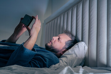 a young man looking at his phone at night in bed