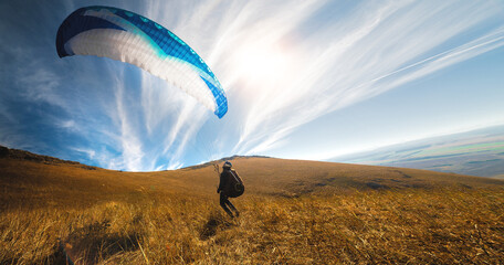 Paragliders take off from a yellow meadow, a man's legs open from the ground, taking off with a...