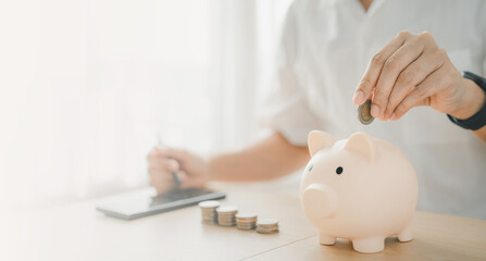 a man hand putting money coin into piggy for saving money wealth and financial concept. Businessman is calculating income and return on investment.