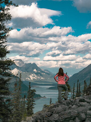 A female hiker stands on the side of a mountain looking at a view of a large reservoir below in...