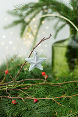 A silver star Christmas ornament hanging on a branch with red berries and greenery in the background. New Year and Christmas concept.