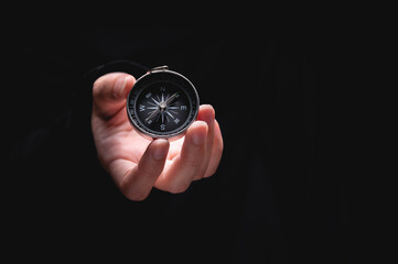 woman hand holds a compass showing south on a black background. A hand from the darkness holds out...