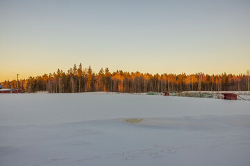 Beautiful winter view of snow-covered stadium against backdrop of forest at sunset. Sweden.