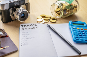 Notebook with Travel Budget and expense list, and next to it camera, glasses, money, calculator....