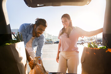 Happy arab couple loading groceries into car at sunset