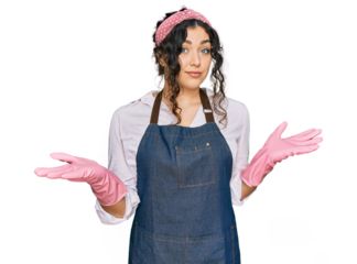Young hispanic girl wearing cleaner apron and gloves clueless and confused expression with arms and hands raised. doubt concept.