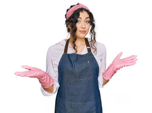 Young hispanic girl wearing cleaner apron and gloves clueless and confused expression with arms and hands raised. doubt concept.