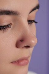 Closeup of a young woman's visage with piercing hanging from her nose.