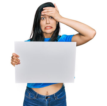Young hispanic woman holding blank empty banner stressed and frustrated with hand on head, surprised and angry face