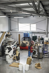 Wide angle view at industrial machines in workshop at small coffee production factory with people working, copy space