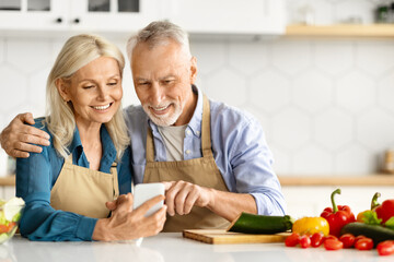 Happy senior couple looking at smartphone screen and cooking together
