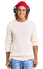 Young hispanic man listening to music using headphones winking looking at the camera with sexy expression, cheerful and happy face.