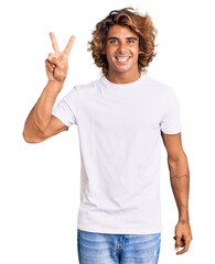 Young hispanic man wearing casual white tshirt smiling looking to the camera showing fingers doing...