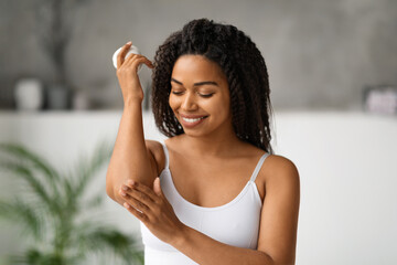 Body Care Concept. Smiling Black Female Rubbing Moisturising Cream On Elbow