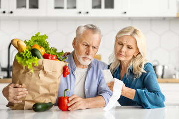 Worried senior couple closely inspecting long grocery receipt after shopping