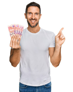 Handsome man with beard holding south african 50 rand banknotes smiling happy pointing with hand and finger to the side