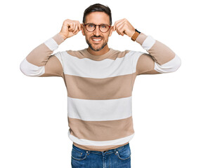 Handsome man with beard wearing casual clothes and glasses smiling pulling ears with fingers, funny...
