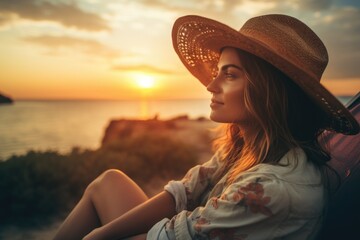 A woman sitting on a beach wearing a hat. Suitable for travel and vacation themes