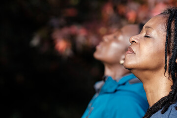 Two black mature women relaxed with closed eyes outdoors. - obrazy, fototapety, plakaty