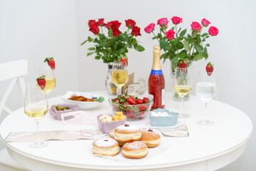 Warmth of Hanukkah. Beautifully Set White Wooden Table with Champagne, Vase of Luscious Strawberries, and Array of Salads, Traditional Sufganiyot-Fluffy Donuts with Powdered Sugar and Delectable Jam.