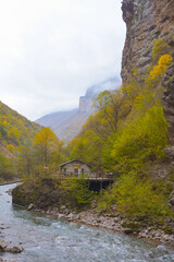 A small house near a mountain river and the foot of the misty mountains. North Caucasus, Russia.