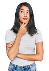 Beautiful asian young woman wearing casual white t shirt with hand on chin thinking about question, pensive expression. smiling with thoughtful face. doubt concept.