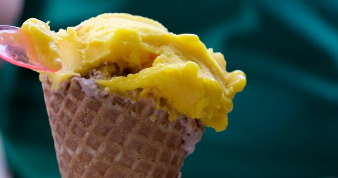 mango ice cream close-up eaten with a plastic pink spoon on a green background in a waffle cup