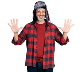 Middle age hispanic man with grey hair wearing fluffy earmuff hat showing and pointing up with fingers number ten while smiling confident and happy.