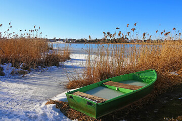 Ein grünes Boot liegt im Winter am Ufer von einem zugefrorenen See