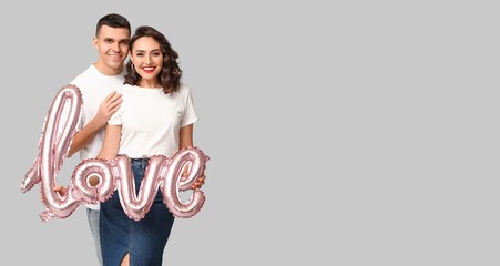 Happy young couple holding balloon in shape of word LOVE on grey background with space for text. Valentine's Day celebration