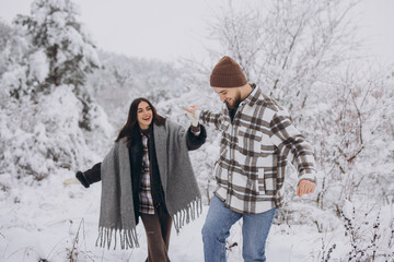 A young happy and loving couple walking in a snowy forest in the mountains