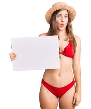Beautiful caucasian young woman wearing bikini holding blank empty banner scared and amazed with open mouth for surprise, disbelief face