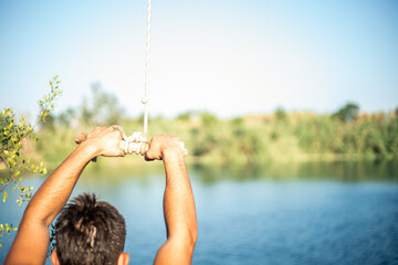 Detail of hands of young Caucasian man grabbing a stick and a rope tied to a tree to jump into the water in a lake. Sunny summer day.