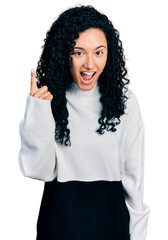 Young hispanic woman with curly hair wearing casual sweater pointing finger up with successful idea. exited and happy. number one.