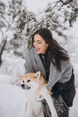 Cute happy woman spending time with akita inu dog in winter in snowy forest